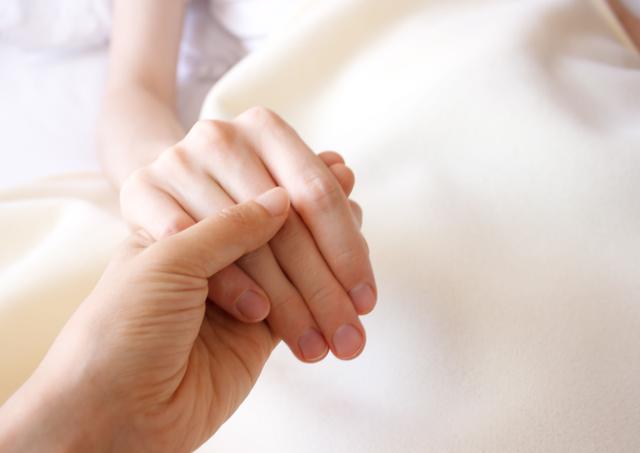 Image of a person holding a patient's hand in a hospital room.