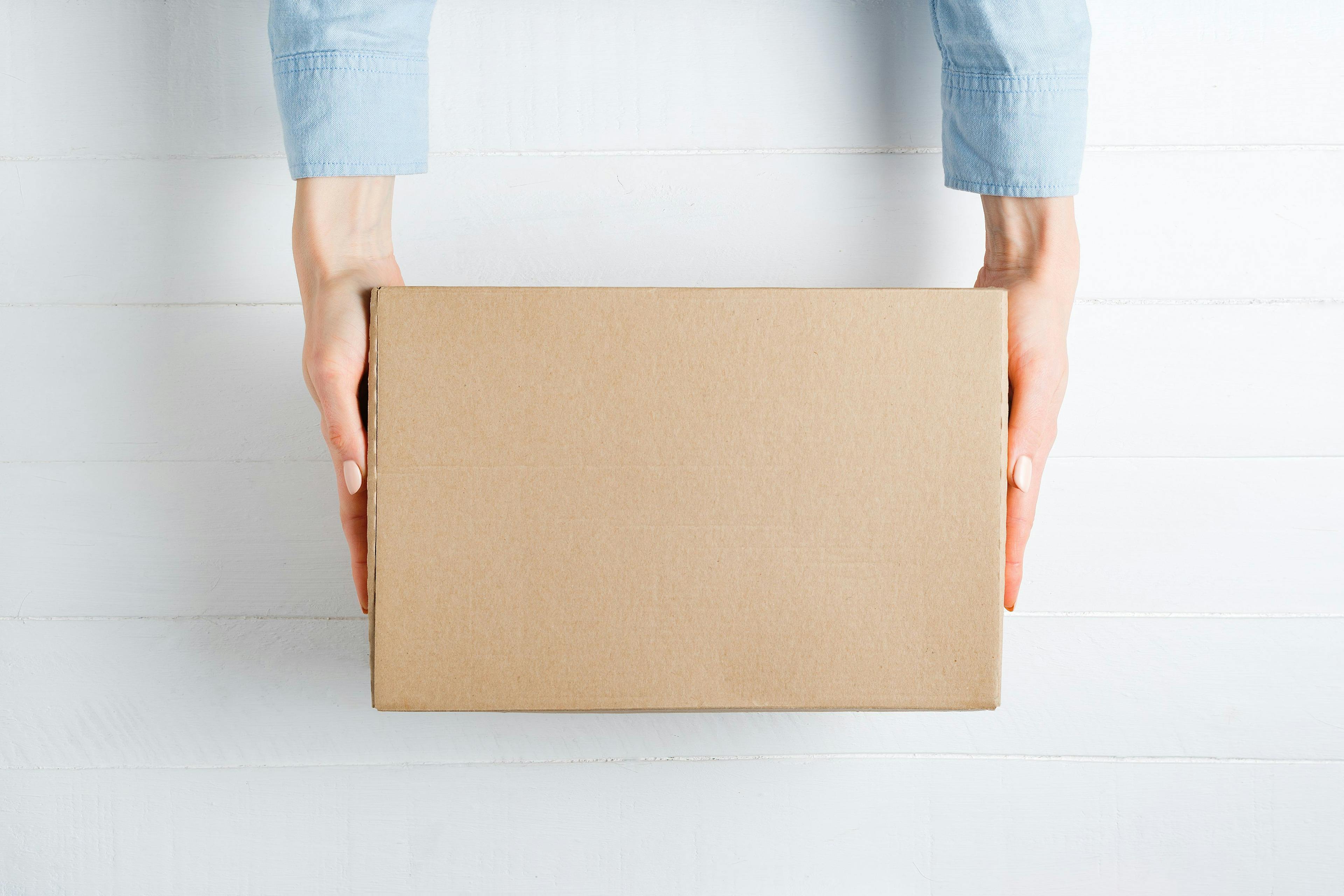Rectangular cardboard box in female hands. Top view, white background | Image credit: © somemeans - © stock.adobe.com