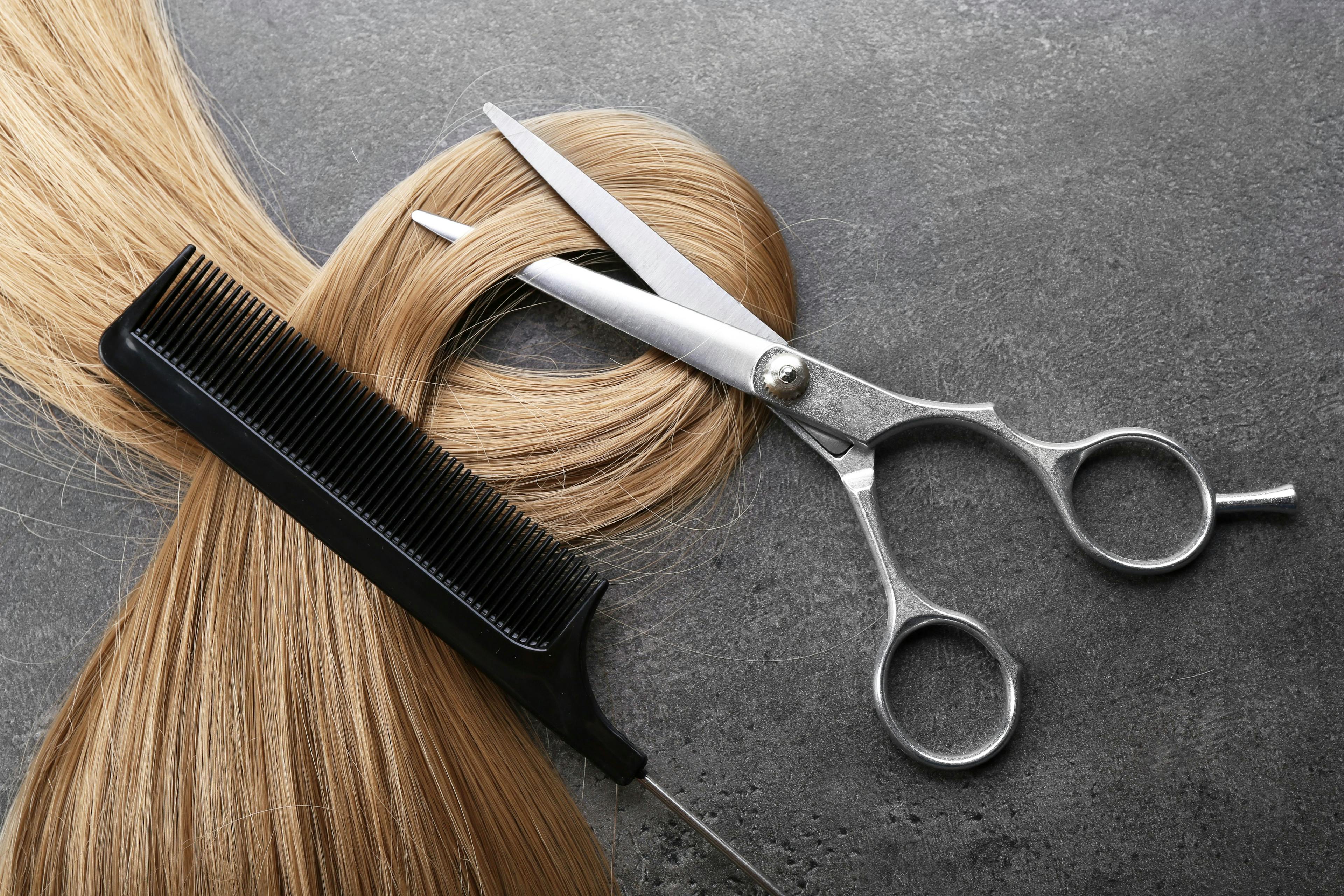 Hairdresser's scissors with comb and strand of blonde hair on grey background | Image credit: © - Africa Studio © - stock.adobe.com