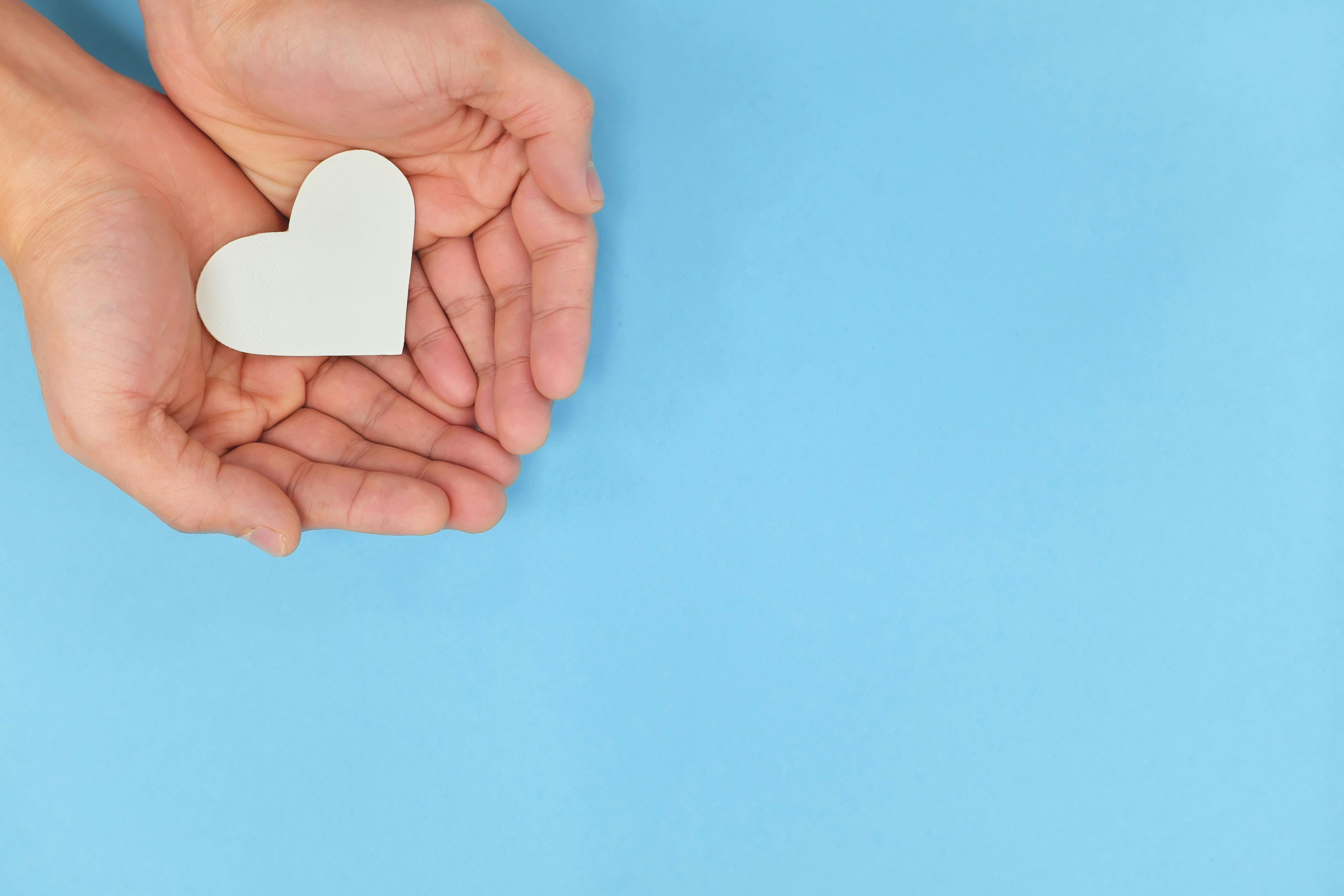 Image of a person holding a paper heart in their hands. 
