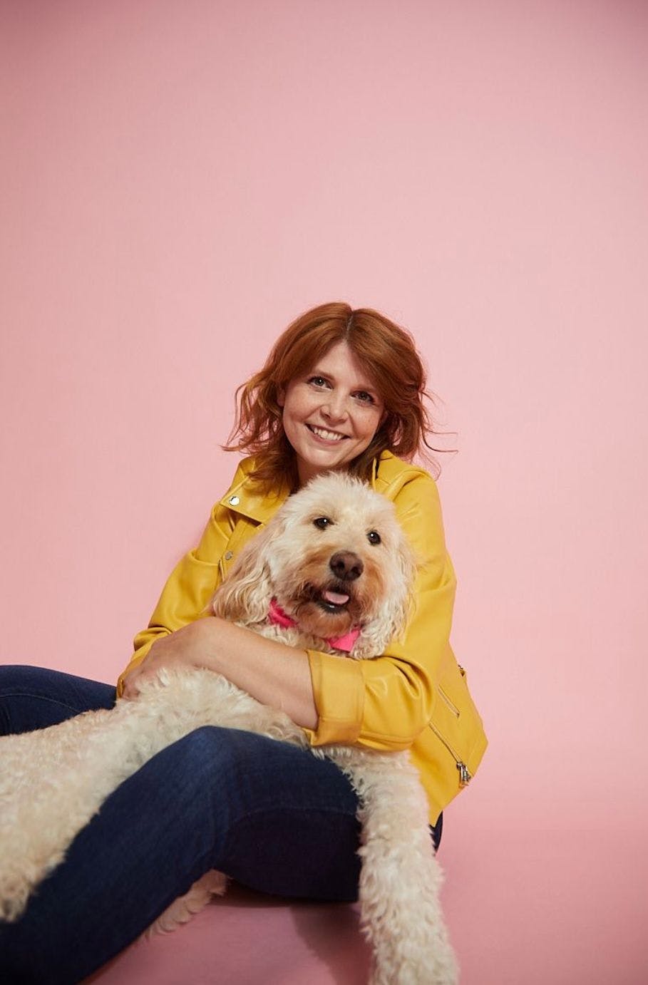 Image of a woman wearing a yellow leather jacket, hugging a dog.  