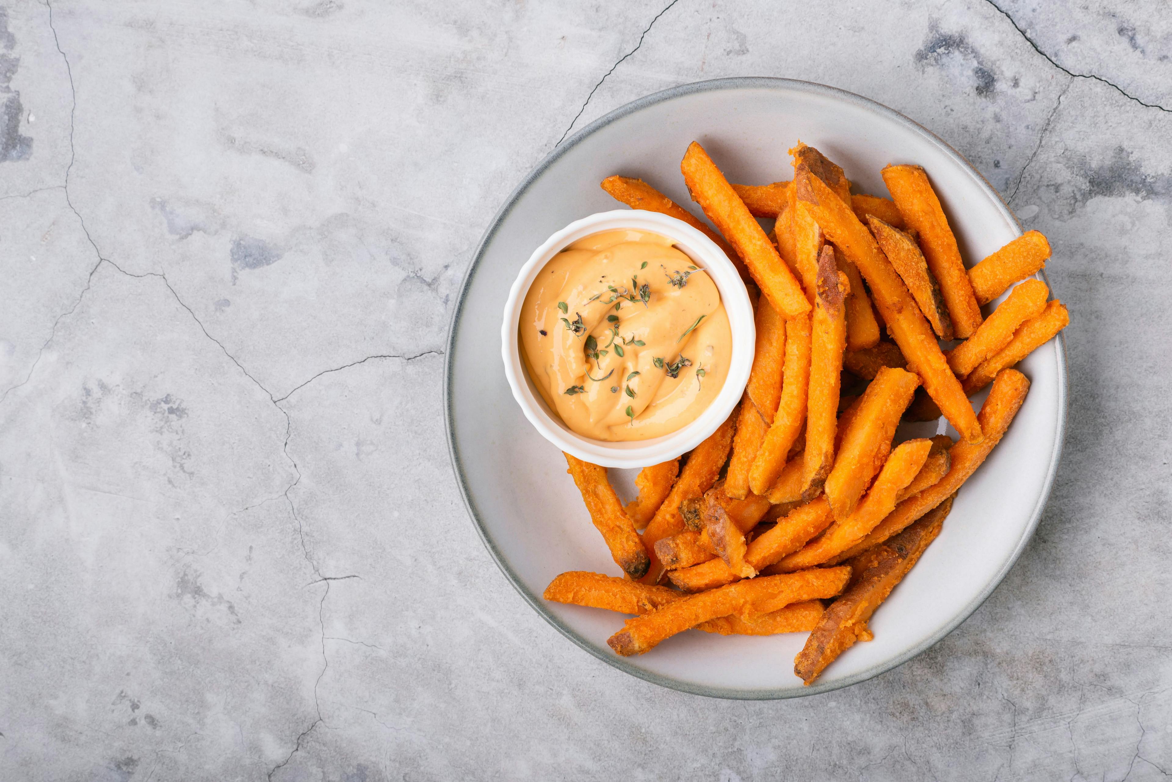 Baked sweet potato fries on a plate with savory sauce over concrete background, top view | Image Credit: © Marina - stock.adobe.com