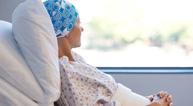 Patient with cancer wearing a headscarf and hospital gown looking out the window.