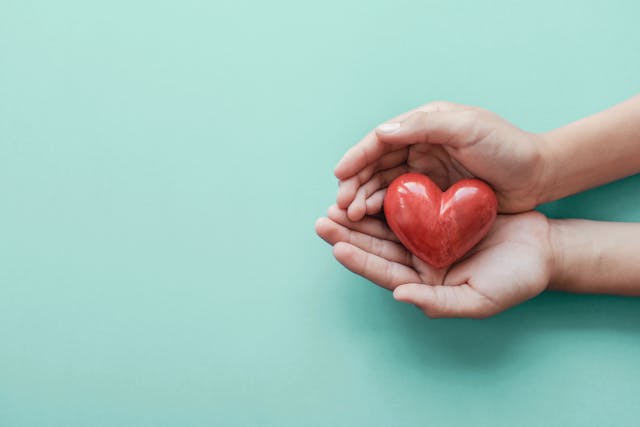 Image of a pair of hands holding a red clay heart.