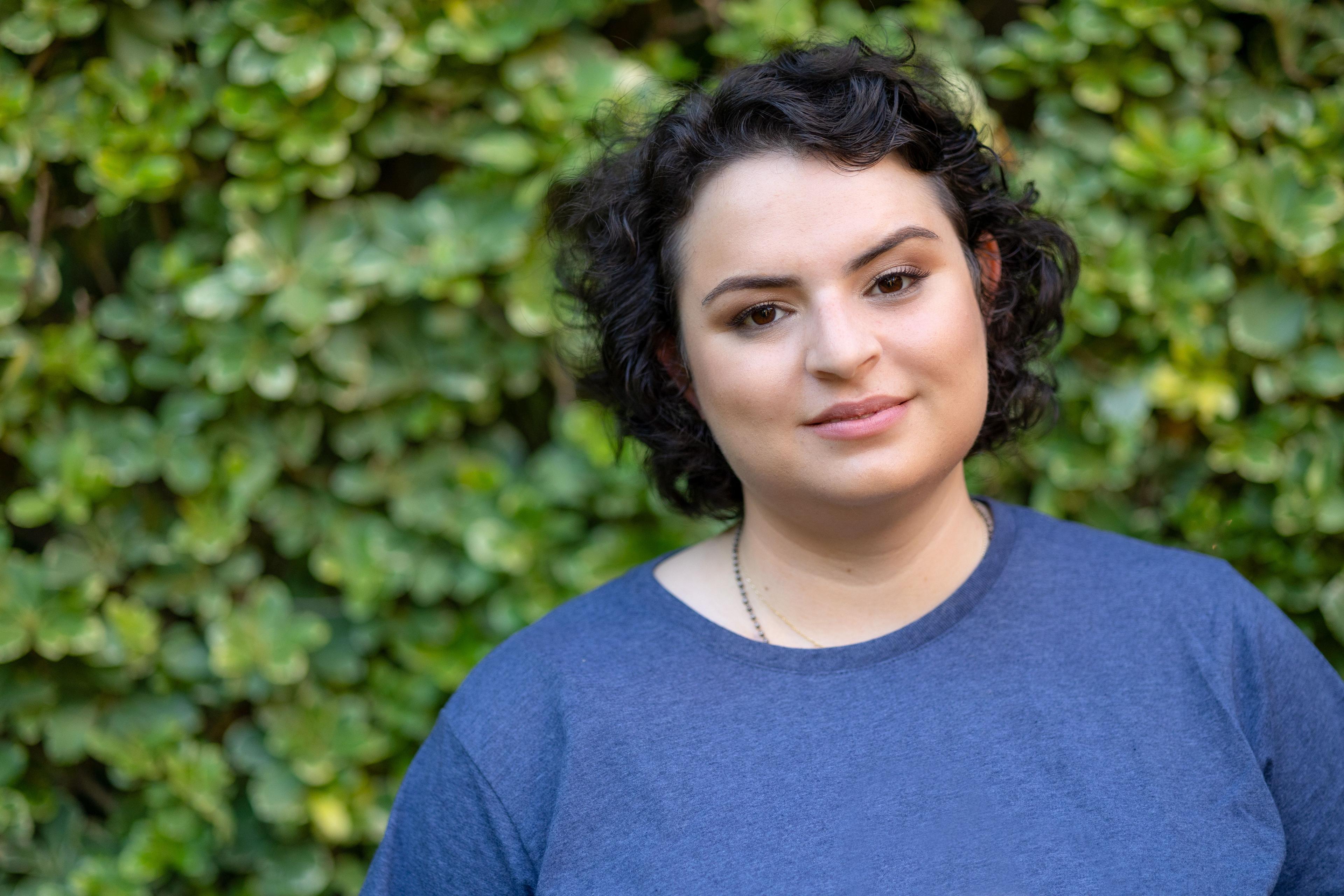 Mia Sandino standing in front of greenery with a blue shirt on