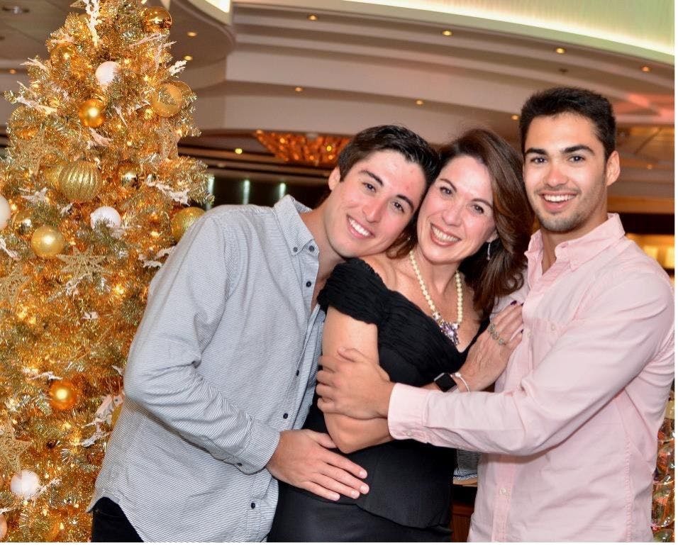 Alex, Debbie and Michael, stand in front of a large Christmas tree hugging and smiling
