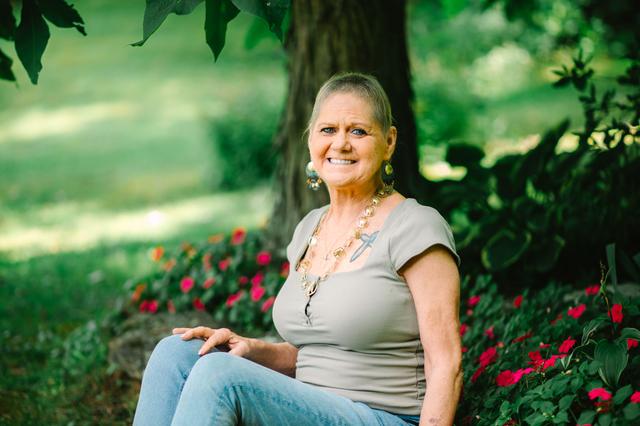 Sabrina Potts in front of a tree with flowers, wearing a khaki-colored shirt and a gold necklace.