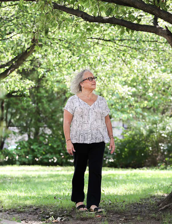 Image of a woman with a white blouse, standing in a park full of greenery.