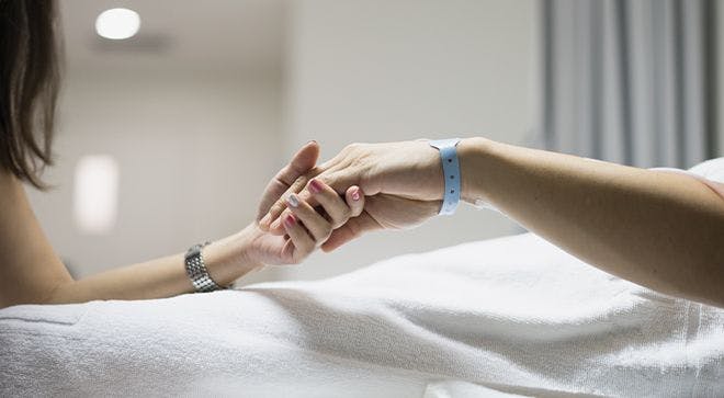 Image of a woman (death doula) holding a patient's hand in the hospital. 
